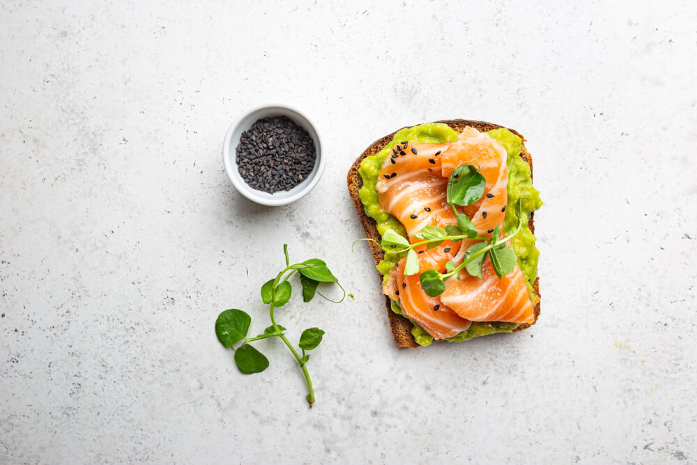 Toast s avokádom, lososom a semienkami na svetlom pozadí